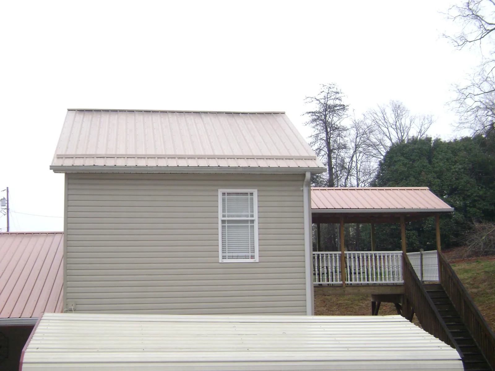 Tan metal roofs on a two story addition and attached porch, from a Roof Replacement job in Lisbon